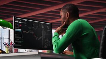 African american man using PC to purchase and sell stocks, monitoring forex graphs and diagrams. Male broker looking at stock exchange candle stick charts on computer. Camera A. video