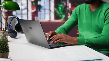 African american teleworker typing ideas to create a vision board on laptop, writing down his dreams and goals aligned with the company objectives. Remote worker connected from his home. Camera B. video