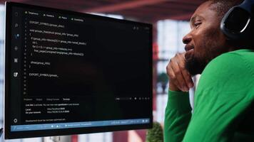 Young IT engineer typing code on computer and running script, programming language. African american technician in modern loft fixing errors within the software, implementing features. Camera A. video