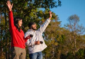 man and woman are standing in a park, holding cups and smiling photo