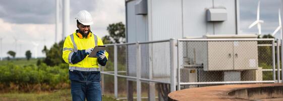 man in a yellow and blue safety vest is looking at a tablet while standing near a fence photo