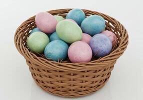Pastel colored painted Easter eggs in a woven basket on straw isolated on white background in clean minimal studio shot with soft shades and spring holiday theme photo