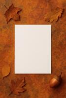 A blank white card surrounded by autumn leaves and an acorn on a textured background, ready for a seasonal message or invitation. photo