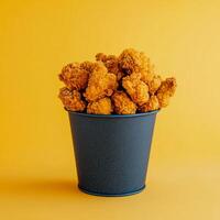 Crispy Chicken Popcorn in a Dark Bucket Against a Yellow Background photo