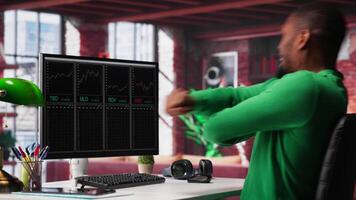 Cheerful day trader gaining money via stock market exchange, maximizing profits by following forex trends and candle stick charts. Thrilled african american broker investor. Camera A. video