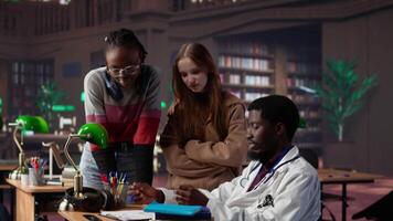Multiethnic group of students in a library participate at a lesson with doctor, using medical books and materials to gain expertise in pharmacology and microbiology. Scientific studies. Camera B. video