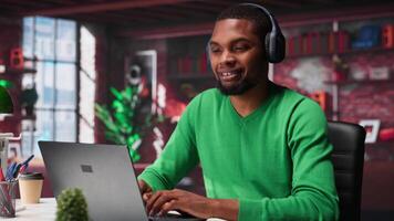 Smiling person in modern loft wearing headphones and listening to music during relaxation time, feeling pleased. Happy guy having fun at home with exciting songs through audio headset. Camera A. video