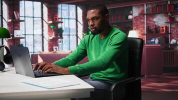 Black man doing remote work feeling uneasy and anxious at desk, shaking his legs and being jittery due to task completion and deadline. Freelancer working under pressure, anxiety. Camera B. video