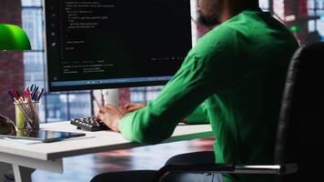 Black technician in home office looks at UI on computer monitor, typing and executing programming code. IT worker using coding application to write and test code in modern apartment. Camera A. video