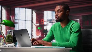 Focused male freelancer browsing web on laptop in a modern studio loft, demonstrating a lifestyle of independence, connection and productivity in a virtual workspace. Man multitasking. Camera A. video