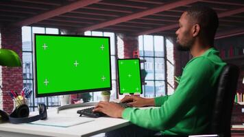 African american person using an isolated display on computer at home, working on his daily assignments on freelancing platforms. Young guy solving tasks from his loft, home setup. Camera B. video