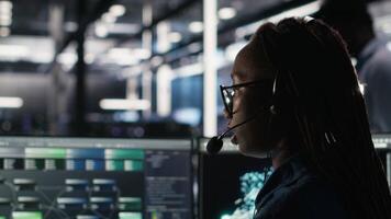 Data center expert examines node tree interface, delivering technical support. Server room technician talking in headset mic with coworkers, using visual programming software, camera B video