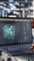 Vertical Close up of data center worker using laptop to interpret data analytics graphs. Server room technician using artificial intelligence on notebook displaying system metrics, camera A video