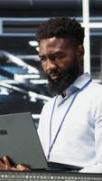 Vertical Portrait of cheerful data center engineer analyzing gear issues using node tree tools. Upbeat African american server hub specialist using AI visualization insights to optimize system health, camera B video