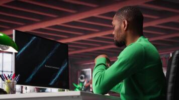 Teleworker in home office watching business conference on PC, looking over statistics charts. African american remote employee in apartment looking at presentation graphs on computer. Camera A. video