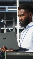 Vertical Data center system administrator analyzing infrastructure issues using node tree tools. Man in server hub using AI visualization insights on laptop to optimize system health, camera B video