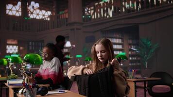 Focused girl arriving at university library and opening textbook to write notes, doing research with the help of massive books database at campus designated space for self learning. Camera B. video
