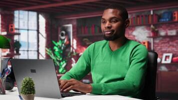 Black teleworker at home desk opening laptop to edit documents and solve daily tasks, updating reports and files. Young employee doing remote job and managing digital paperwork. Camera A. video