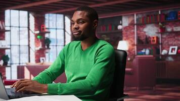 Black teleworker at home desk opening laptop to edit documents and solve daily tasks, updating reports and files. Young employee doing remote job and managing digital paperwork. Camera B. video
