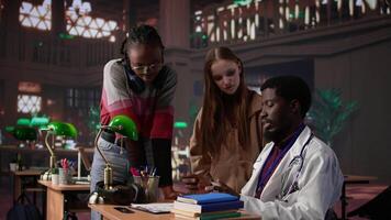 Diverse group of pupils in a library discuss with a medic resident, preparing for a new lecture at med school. Using medical books and materials to gain expertise in microbiology. Camera B. video