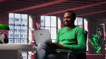 African american guy in loft opening laptop in the morning to work, browsing internet and researching information online. Teleworker starting job shift, using search engine on pc. Camera A. video