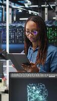 Vertical Portrait of smiling server room engineer using device to interpret data analytics graphs. Happy data center worker using artificial intelligence tool showing system metrics, camera A video
