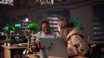 Young scholar focuses on exam preparations in the campus library with colleague, takes notes on laptop from reference books in a peaceful study setting. Girl uses the database materials. Camera B. video