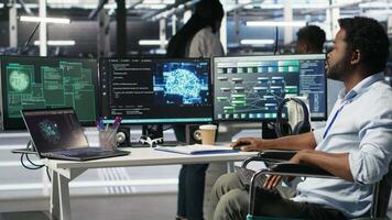 Data center engineer in wheelchair using AI requesting help from coworkers during security breach. Server farm worker with disability aided by colleagues to fight hacker attack stealing data, camera B video