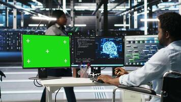 Data center admin in wheelchair using AI node tree software on green screen PC to minimize system downtime. Server hub employee in disability using visual programming tool on mockup computer, camera B video