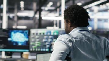 Server room programmer with paraplegia interprets data analytics graphs. Man in wheelchair using artificial intelligence program showing predictive system metrics in data center, camera B video