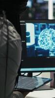 Vertical Data center engineer in wheelchair and colleague oversee automated tasks using node tree programming tool. Inclusive server farm team adjusts system settings based on AI analytics, camera B video