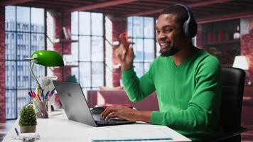 Smiling person in modern loft wearing headphones and listening to music during relaxation time, feeling pleased. Happy guy having fun at home with exciting songs through audio headset. Camera B. video
