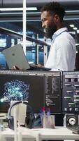 Vertical Data center system administrator analyzing infrastructure issues using node tree tools. Man in server hub using AI visualization insights on laptop to optimize system health, camera A video
