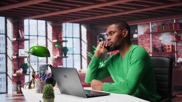 Freelancer in home office having important phone call with business partner using his mobile phone. African american guy sitting at desk discussing company matters during call. Camera A. video