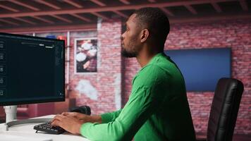 Black graphic designer working in loft with AI image generator software. Digital screen displaying visuals created through machine learning and cloud computing, . Camera B. video