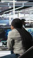 Vertical Server room specialist applies artificial intelligence technology to minimize system downtime. African American worker develops and deploys AI solutions to optimize data center equipment, camera A video