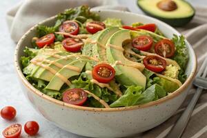 Fresh organic salad with avocado, cherry tomatoes, and creamy dressing, beautifully arranged in ceramic bowl, perfect for healthy meal photo