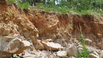 An erosion of soil and rock layers reveals rugged landscape with exposed stones and roots, showcasing natural processes of earth movement and vegetation growth photo