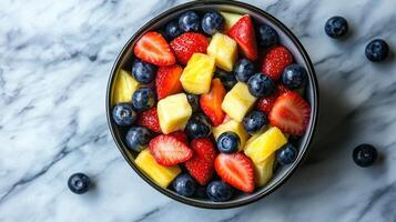 Fresh fruit bowl with strawberries, pineapples, and blueberries on a marble surface in natural light photo