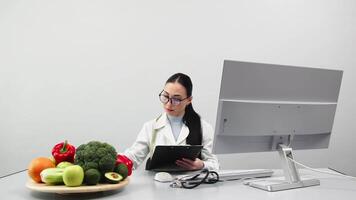 weiblich Ernährungsberater Arbeiten im ein modern Klinik auf ein Licht Hintergrund beim ein Computer in der Nähe von frisch Gemüse und Früchte. Konzept von gesund Essen, Vegetarismus und Gewicht Verlust video
