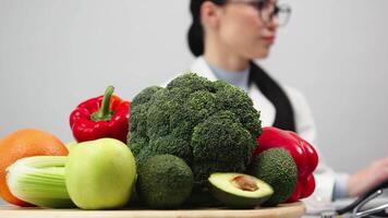 weiblich Ernährungsberater Arbeiten im ein modern Klinik auf ein Licht Hintergrund beim ein Computer in der Nähe von frisch Gemüse und Früchte und suchen beim das Kamera. Konzept von gesund Essen, Vegetarismus und Gewicht Verlust video