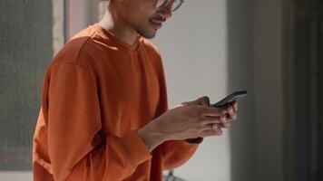 African American student guy male man schoolboy chatting with mobile phone smartphone addition playing game virtual app social media scrolling modern technology relaxing in university college corridor video