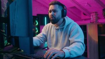Emotional Caucasian addicted male gamer guy man streamer play at computer internet virtual gaming talking to microphone in headphones angry talk smiling emotion at home web battle online game video