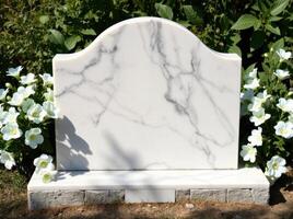 A white marble headstone in front of some flowers photo