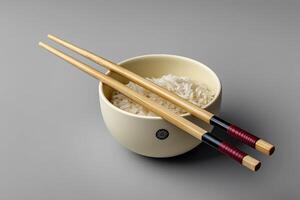 Chopsticks resting on a ceramic holder beside a bowl of rice on a minimalist surface photo