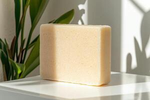 Natural soap block displayed under sunlight with indoor green plant in the background photo