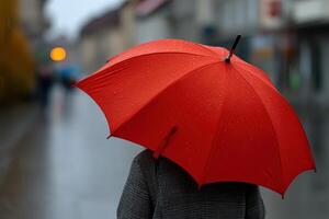 Vibrant red umbrella contrasts with rainy street in urban setting during gloomy weather photo