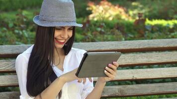 Teenage girl joyfully browsing on a tablet while sitting on a park bench video