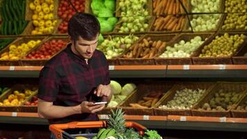 Smiling guy checks smartphone while shopping for fresh produce video