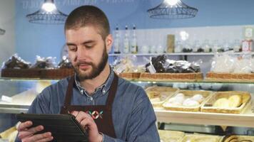 Cheerful male baker engaging with customers using a digital tablet video